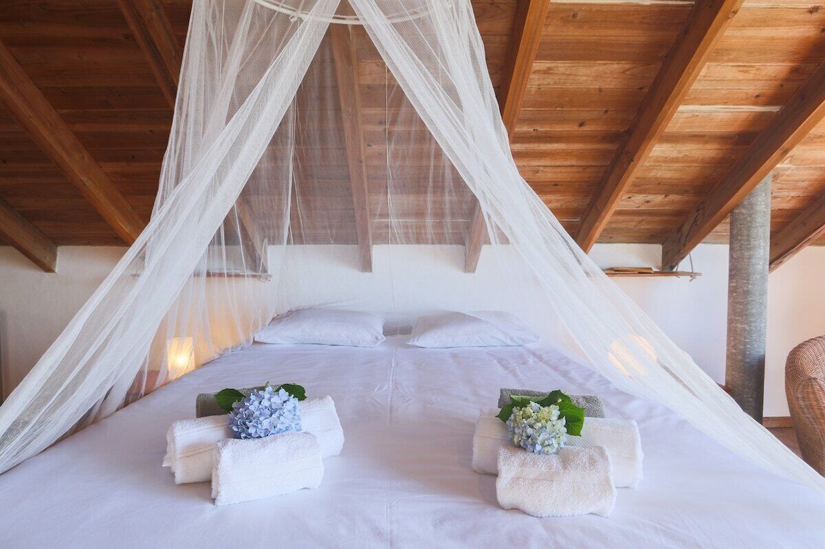 Una cama con sábanas blancas, dosel y dos toallas con flores.