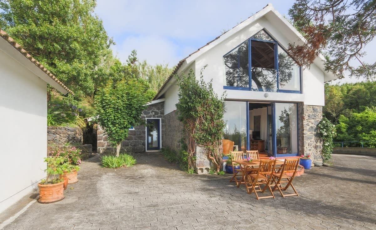 Una casa moderna de dos pisos con fachada de piedra, ventanas amplias y un patio con mobiliario exterior.