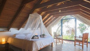 Un dormitorio con techo de madera, una cama con dosel, una mesita de noche, una silla y vistas al exterior.