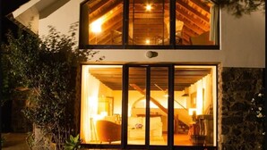 Una casa de dos pisos con techo inclinado y un gran ventanal que da a un interior con escalera y sofá.