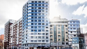 A modern multi-story building with a mix of residential and commercial spaces, featuring a prominent glass facade and a central entrance.