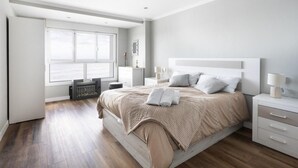 A modern bedroom with a large bed, bedside tables, a radiator, and a window with a view.