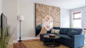 Un soggiorno con un divano blu scuro, un tavolino rotondo, una lampada da terra e un grande quadro astratto appeso al muro.