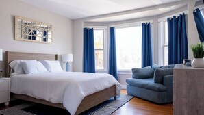 Una camera da letto con un letto, un comodino, un divano blu e una finestra con tende.