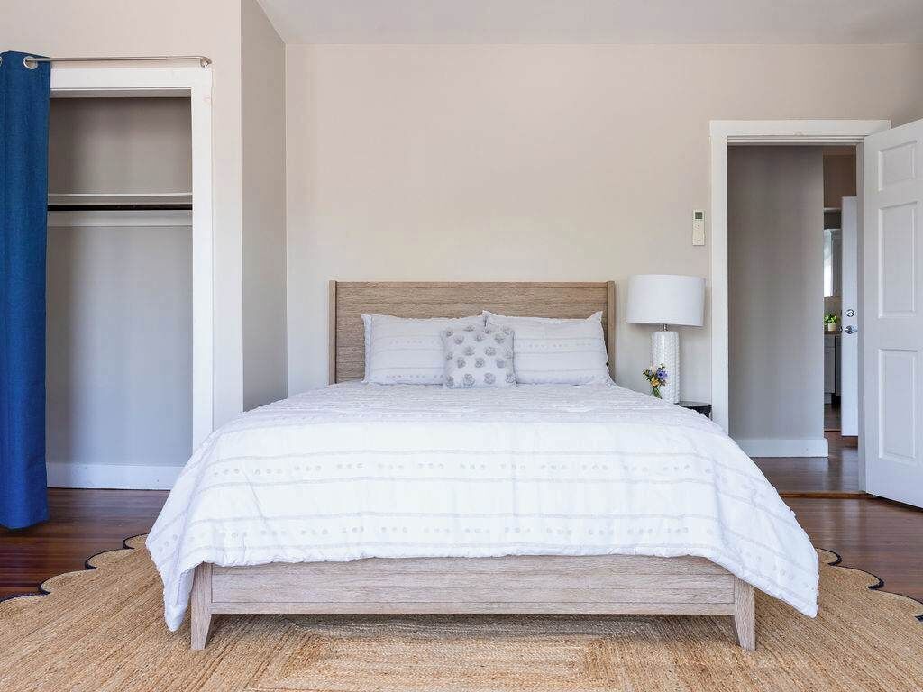 A bedroom with a bed, a nightstand, a lamp, a wardrobe, and a door.