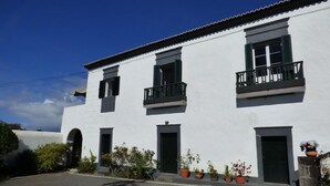 A white building with three balconies, a central door, and potted plants.
