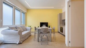 A modern living room with a sofa, dining table, chairs, and a TV. - Domus Mameli Apartment C (Cagliari)