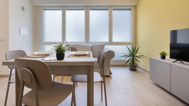 A modern living room with a dining area, a sofa, a TV, and a large window. - Domus Mameli Apartment C (Cagliari)