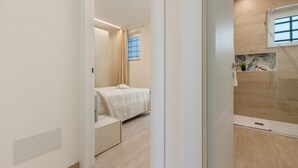 A modern hotel room with a bed, a small seating area, a shower, and a window with blinds. - Domus Mameli Apartment C (Cagliari)