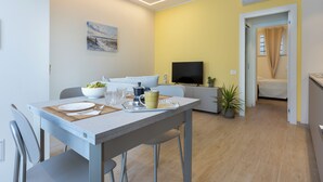 Een moderne woonkamer met een eethoek, een flatscreen televisie en een gele accentmuur.