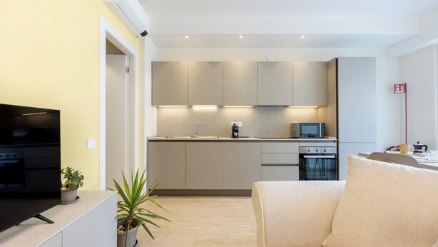 Een moderne keuken met inbouwapparatuur, een flatscreen televisie en een zithoek met een bank.
