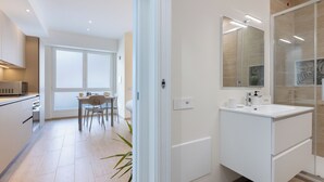 Een moderne keuken met witte kasten, een eethoek met tafel en stoelen, en een groot raam.