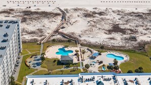 An aerial view of a resort with a beach, two swimming pools, and a parking area.