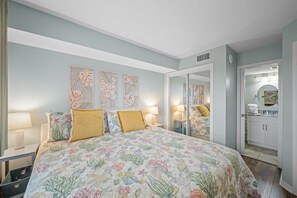 Un dormitorio con cama, mesitas de noche, un espejo y un baño visible a través de una puerta abierta.
