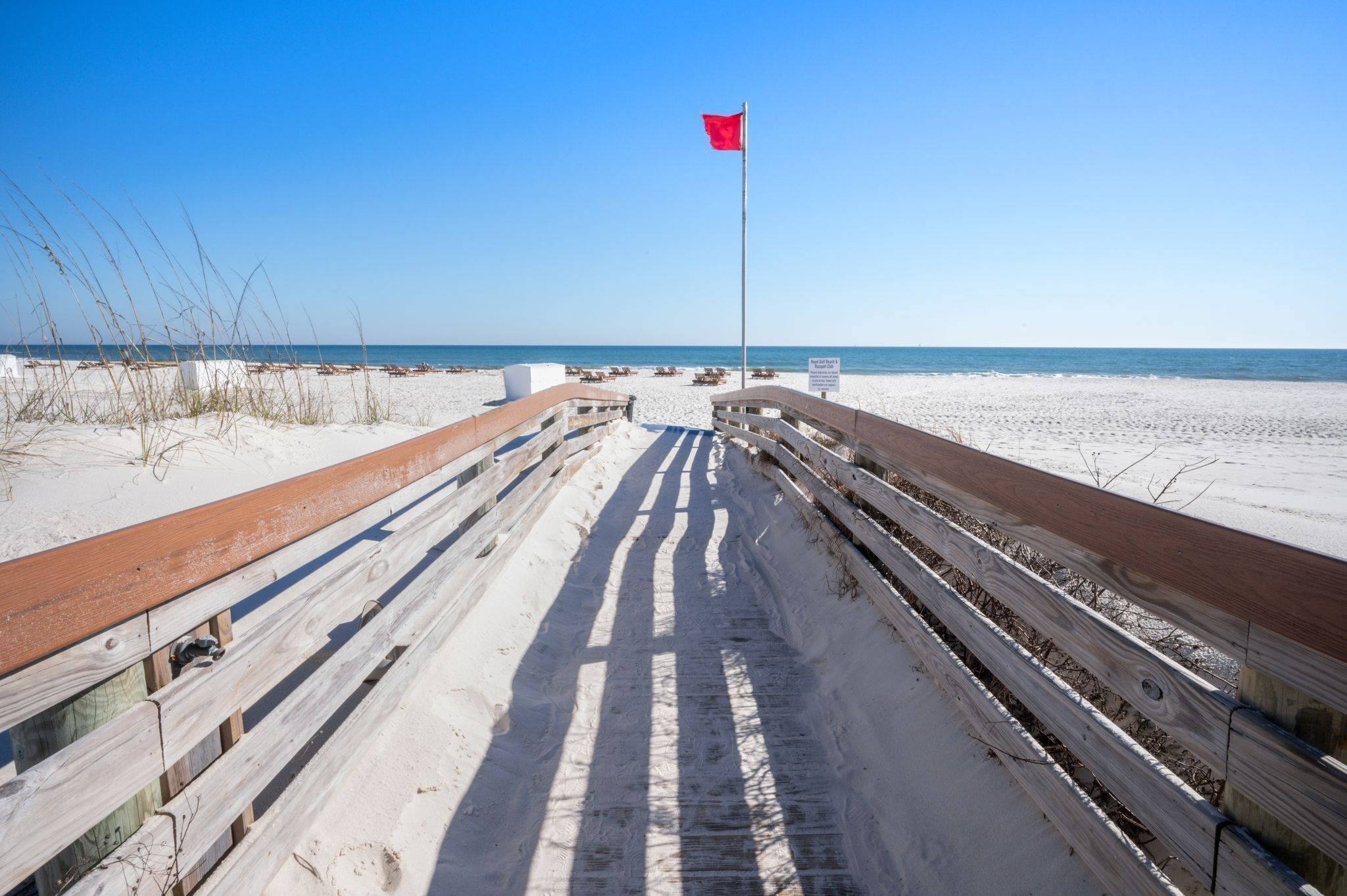 Ein Strandweg mit roter Flagge, Holzgeländern und freiem Blick auf den Ozean.
