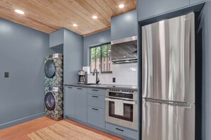 A modern kitchen with grey cabinetry, stainless steel appliances, and a wooden ceiling. - Casita Atala - Nestle into a Tropical Designer Retreat with Shared Pool (West Palm Beach)