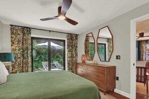 A bedroom with a bed, a dresser, a ceiling fan, and a view of a garden through a sliding door. - Casita Atala - Nestle into a Tropical Designer Retreat with Shared Pool (West Palm Beach)