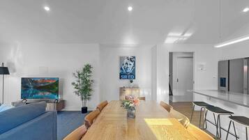 Un salon moderne avec une table à manger en bois, un canapé bleu et un téléviseur diffusant un paysage de montagne.