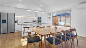 A modern kitchen with white cabinets, a stainless steel refrigerator, and a wooden dining table with chairs. - Sunny Home Minutes to Remarkables Ski Field (Queenstown)