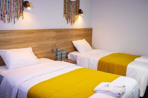 A hotel room with two beds, wooden headboard, white bedding, yellow bedspreads, wall-mounted lights, and a small table with water bottles. - Hotel Litan Machu Picchu (Aguas Calientes)