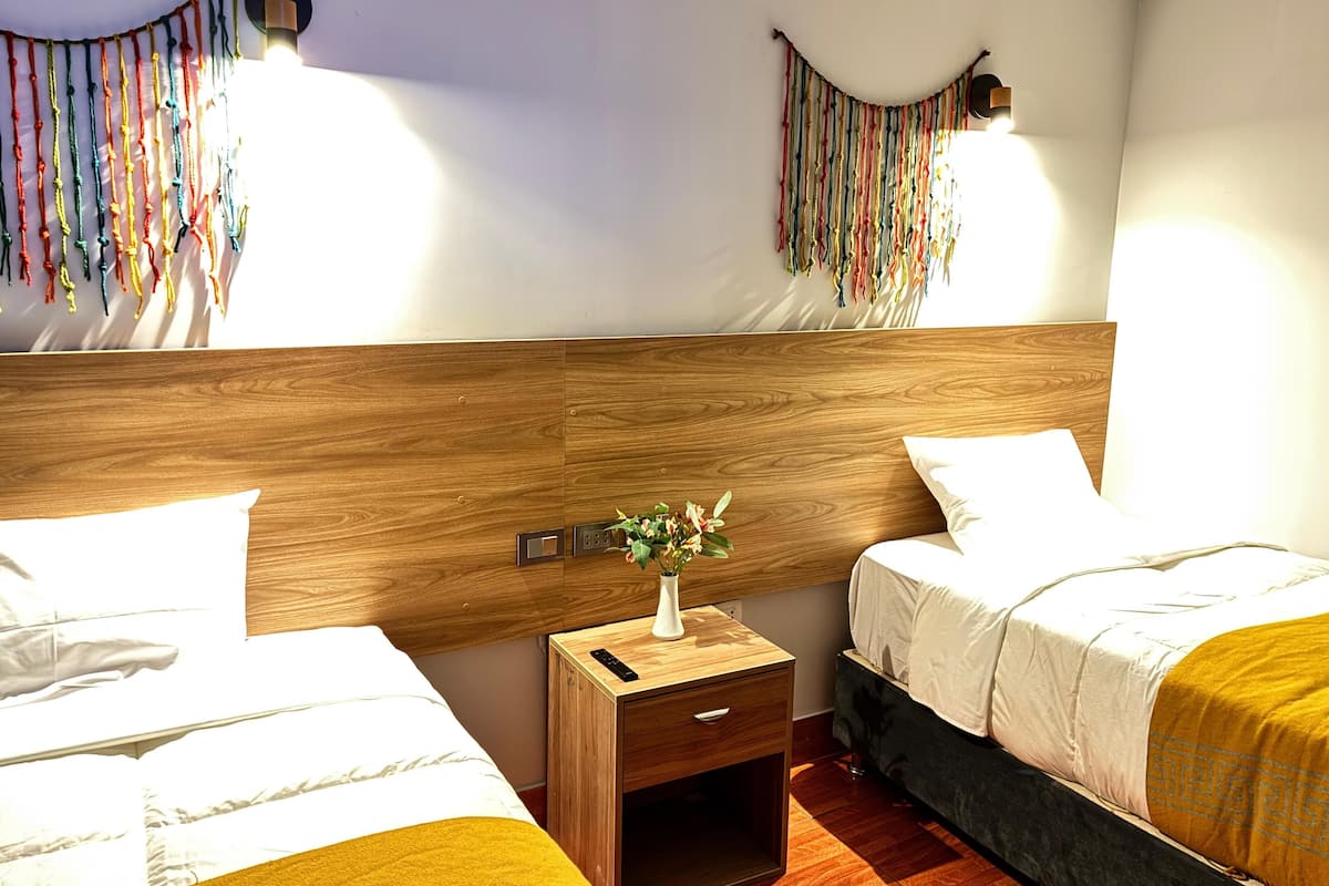 A hotel room with two beds, wooden headboard, bedside tables with lamps, and colorful wall decorations.