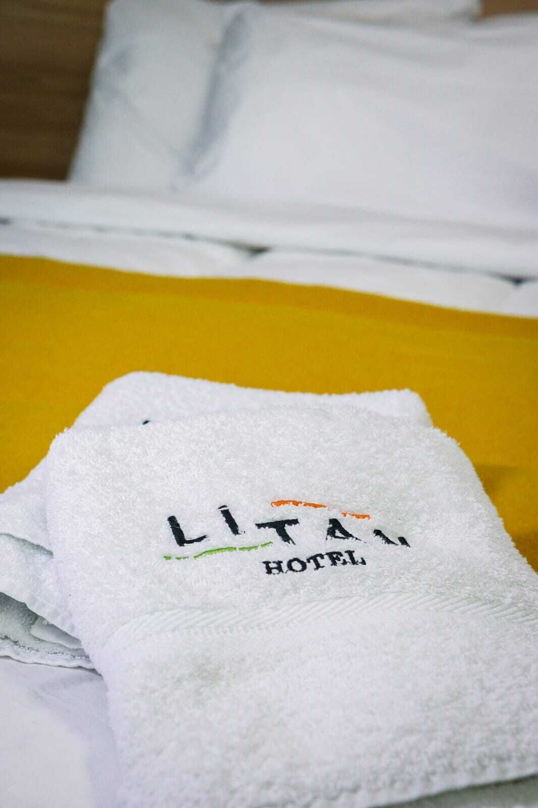 Una toalla blanca con el bordado 'LITANI HOTEL', sobre una superficie amarilla, probablemente una cama.