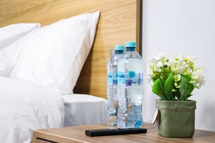 Une chambre d’hôtel avec un lit, des oreillers, une table de chevet avec des bouteilles d’eau, une télécommande et une plante en pot.