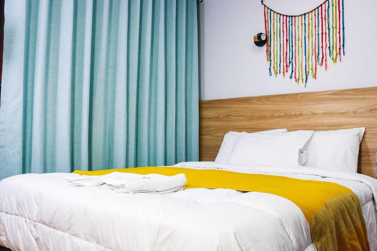 A bed with white bedding and a yellow throw, a wooden headboard, and teal curtains.