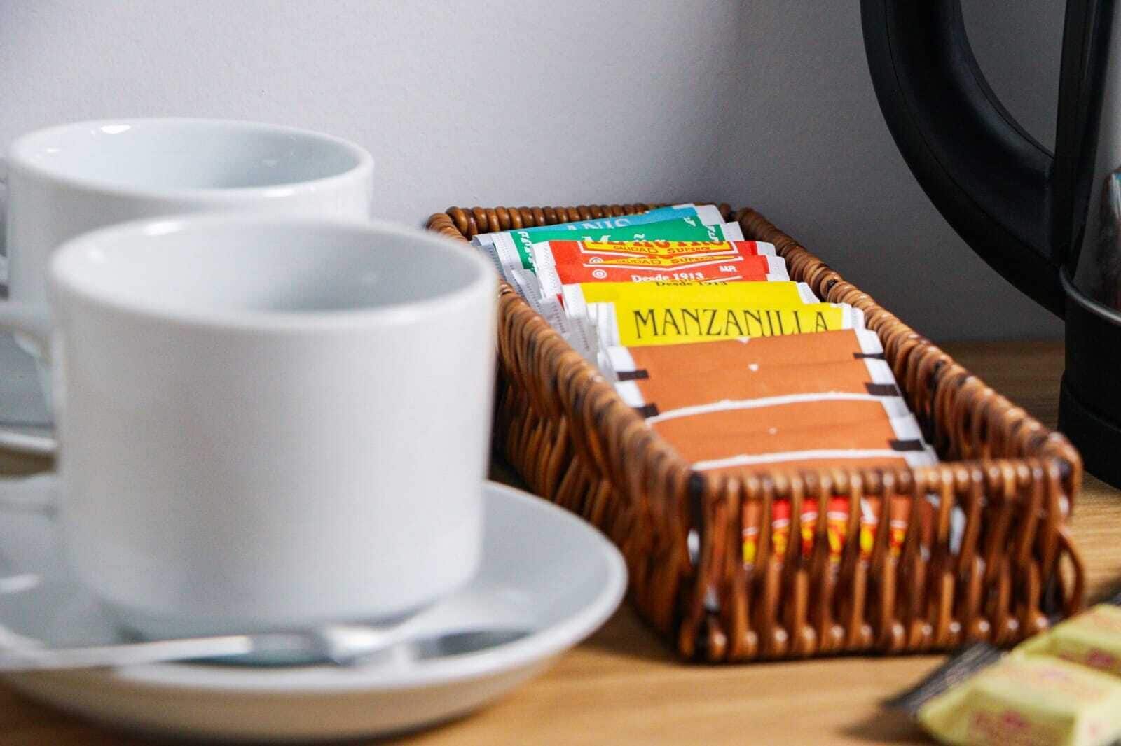 A wicker basket containing Manzanilla beer boxes, a white mug, and a plate with a spoon on a wooden table.