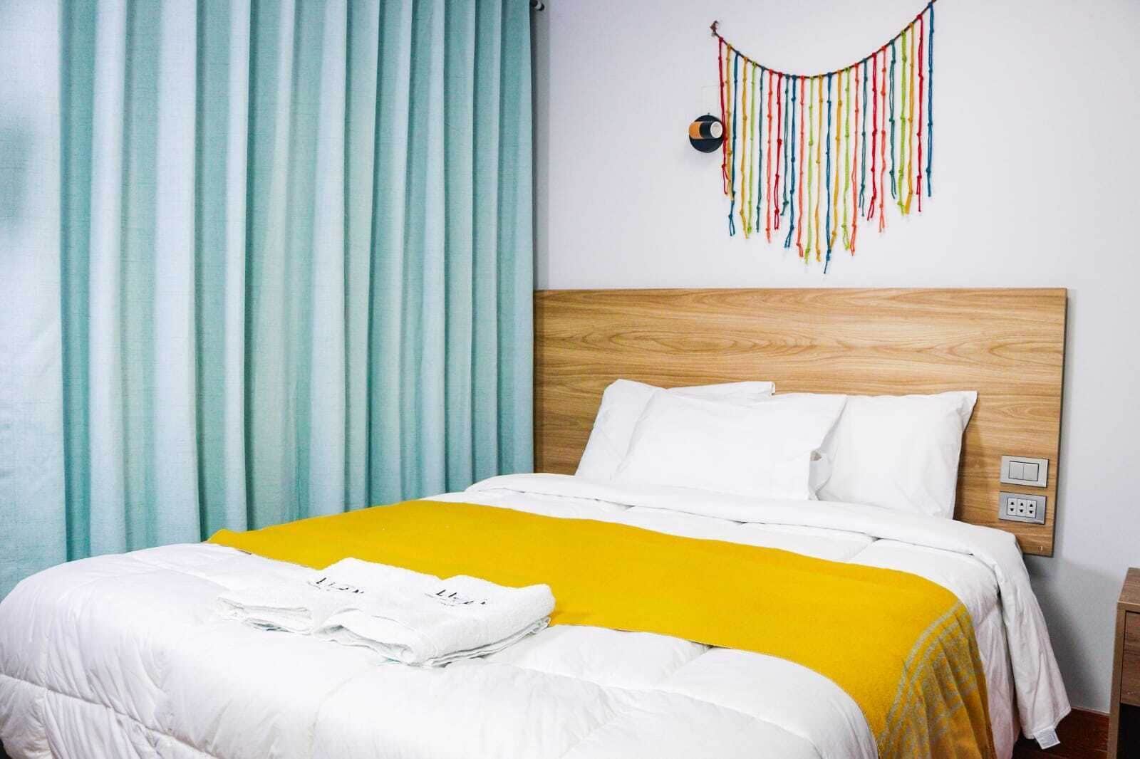 A hotel room with a wooden headboard, white bedding, a yellow accent, and a wall decoration.