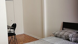 Ein schlichter, einfach eingerichteter Raum mit einem Bett, einem Stuhl und einem Schreibtisch.
