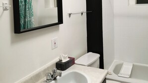 Ein Badezimmer mit einem weißen Waschbecken, einer Toilette und einer Badewanne. Über dem Waschbecken befindet sich ein Spiegel und eine Handtuch an der Wand.
