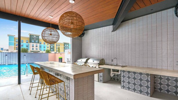 An outdoor kitchen area with a bar stool seating, a grill, and a view of a swimming pool.