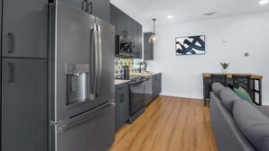 A modern kitchen with stainless steel appliances, a dining area with a sofa, and a wall-mounted artwork.