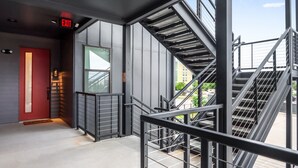 A modern building interior with a red door, a staircase with metal railings, and a clear view of the sky through large windows.