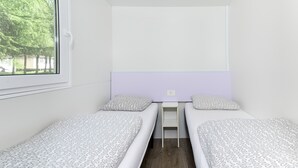 Una habitación pequeña y moderna con dos camas individuales, una ventana y vistas a árboles.