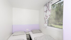 A small, single-room accommodation with two single beds, a window with a view of greenery, and a simple, functional design. - Camping 2000 - Stacaravan Fiji (Osecná)