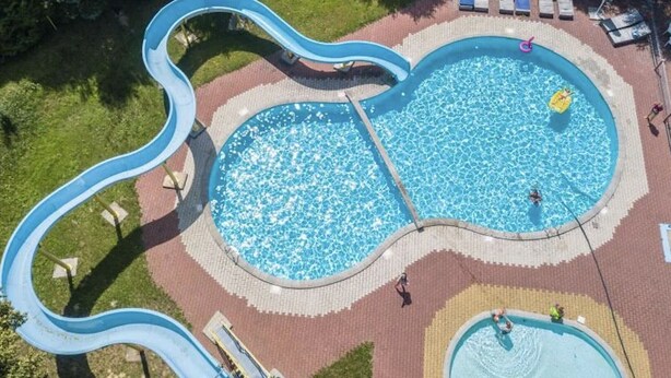 A swimming pool with a slide, surrounded by a brick pathway and lounge chairs. - Camping 2000 - Stacaravan Fiji (Osecná)