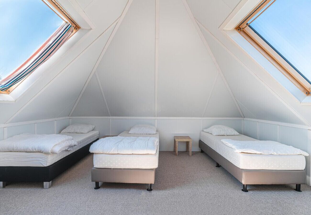 Une chambre mansardée de forme triangulaire, avec trois lits, une petite table et des fenêtres de toit.