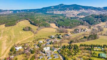 An aerial view of a small village with houses and fields, surrounded by hills and a mountain in the background.