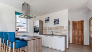 Une cuisine moderne dotée d’un îlot central, de tabourets de bar, d’un four encastré et d’une porte en bois.
