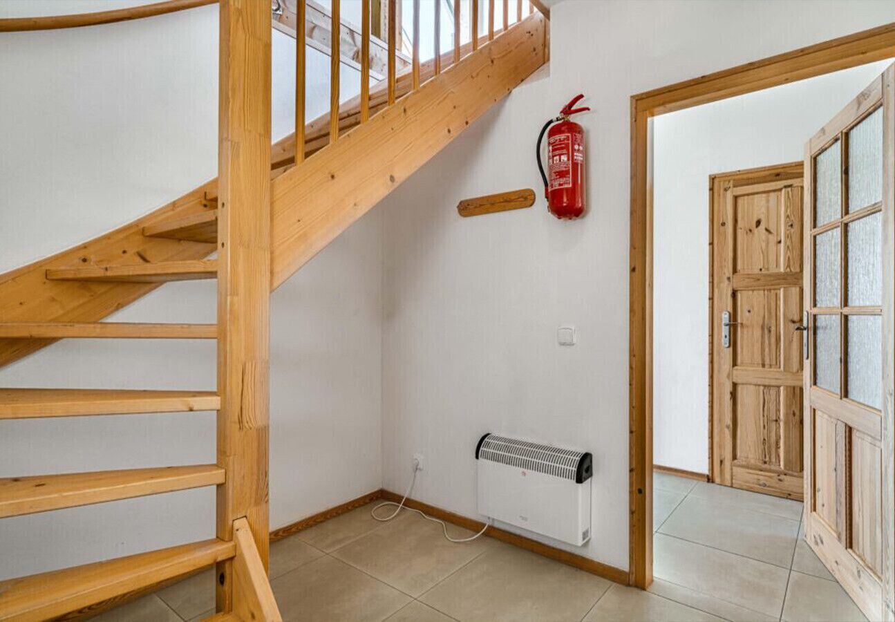 Una scala in legno conduce a un pianerottolo, con un estintore montato sulla parete e una porta in legno.