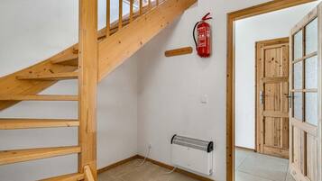 Una scala in legno conduce a un pianerottolo, con un estintore montato sulla parete e una porta in legno.