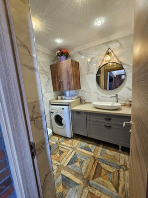 A bathroom with a marble floor, a washing machine, a sink, and a wooden cabinet above the mirror. - ARİFE REZİDANCE NO.2 (Didim)