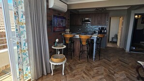 A spacious living area with a herringbone wood floor, a ceiling fan, and a kitchen in the background. - ARİFE REZİDANCE NO.2 (Didim)