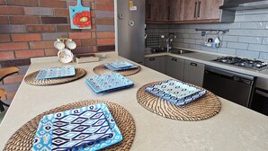 A modern kitchen with a brick wall, wooden cabinets, a stainless steel refrigerator, and a countertop with woven placemats. - ARİFE REZİDANCE NO.2 (Didim)