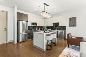 A modern kitchen with stainless steel appliances, a central island with bar stools, and a hanging light fixture.