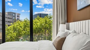 A hotel room with a large bed, a window with a view of buildings and trees, and a curtain. - Lux Mocha Downtown Self Check-in Balcony (Atlanta)