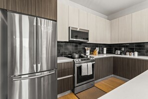 A modern kitchen with stainless steel appliances, dark wood cabinets, and black tiled backsplash.