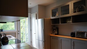 A modern kitchen with a refrigerator, microwave, and toaster. There is a window with a view of greenery outside. - ROSEMONT: Nice apartment 2 steps from Molson Park! (Montréal)